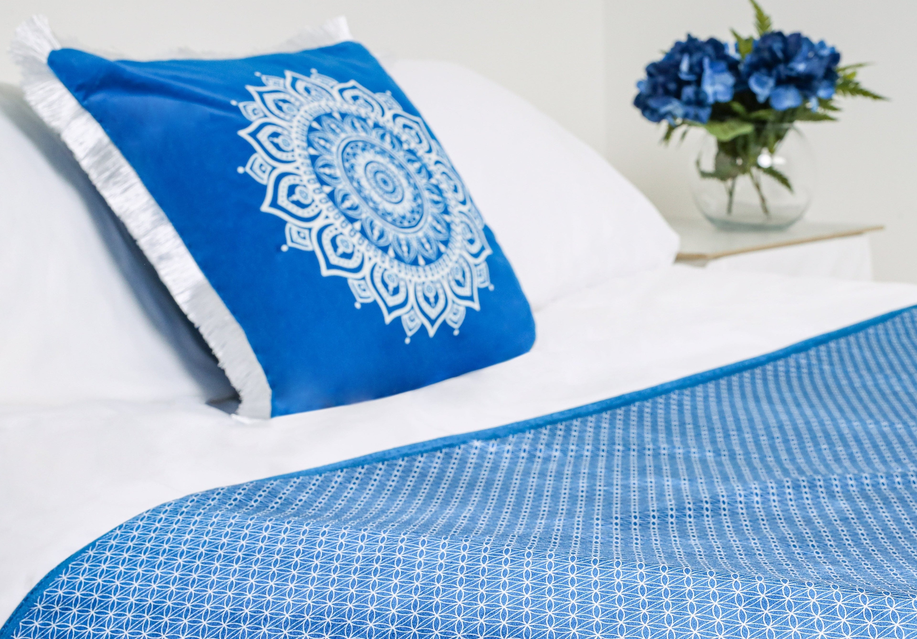 A blue geometric bed runner on a white bed styled with a blue mandala cushion