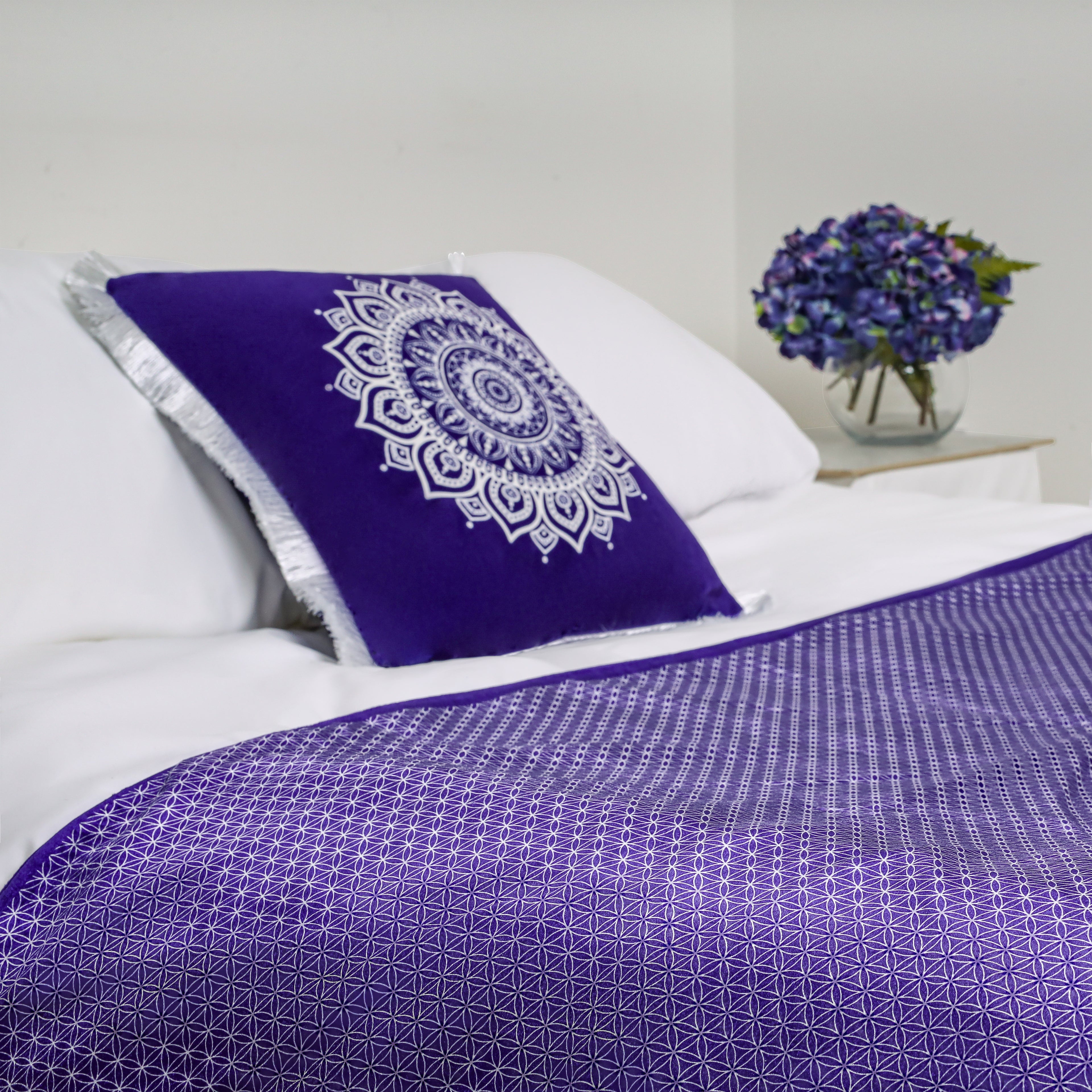 A purple geometric bed runner on a white bed styled with a purple mandala cushion